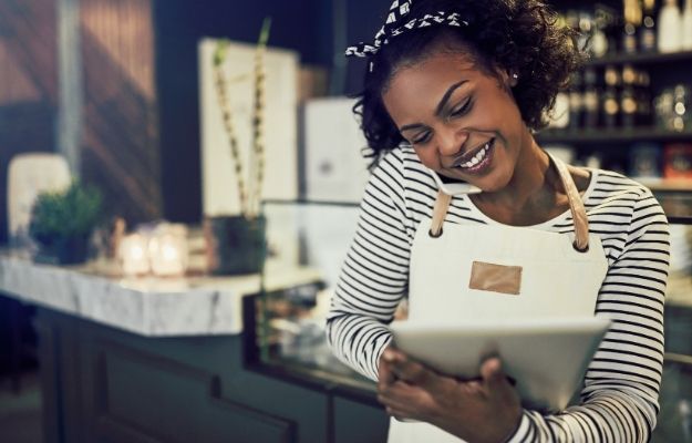 Black Girl in a shop while on her phone and holding a tablet - - Should I Add the Black-Owned Attribute | How to Add a Black-Owned Business Attribute to Your Google Maps