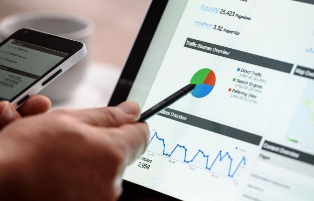 Person holding a phone while pointing at a computer screen showing charts and number with a pen - Utilize SEO for the Best Result | Utilize SEO for the Best Result | 3 Franchise Marketing Ideas to Boost Local Business