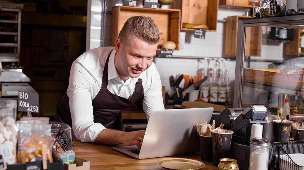 cafe worker in brown apron using a laptop