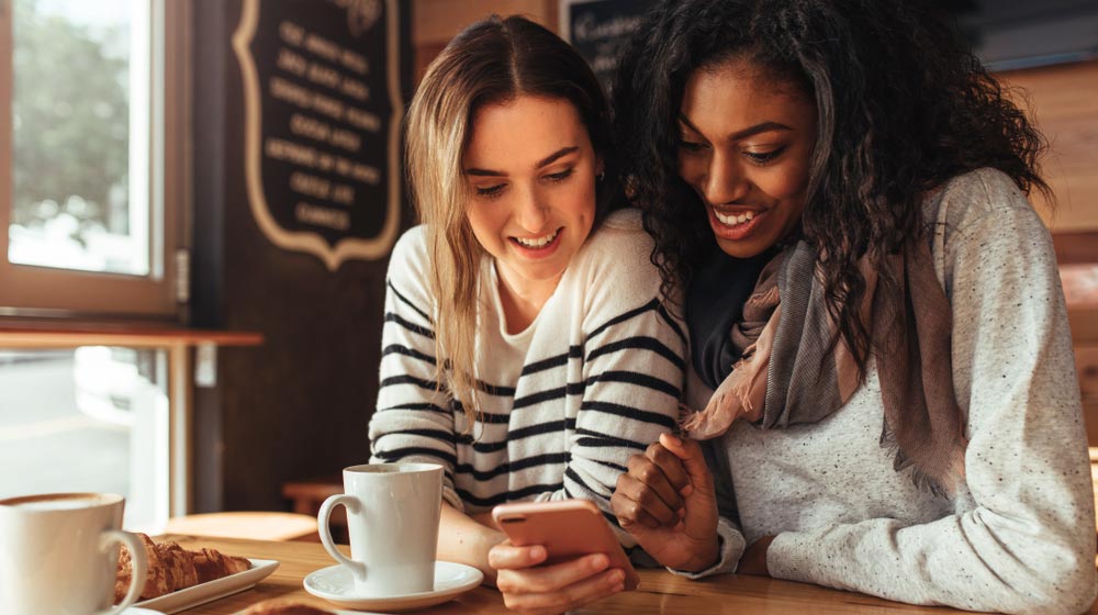 Two people caucasian-black-scrolling-on-phone-while-having-breakfast-in-coffee-shop