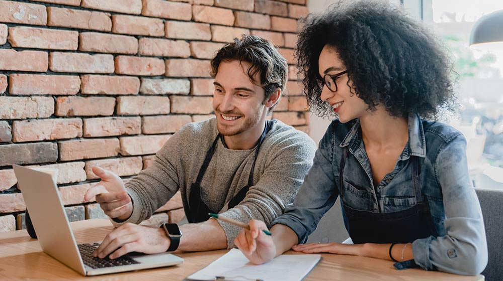 A woman and a man looking at a laptop in front of a brick wall