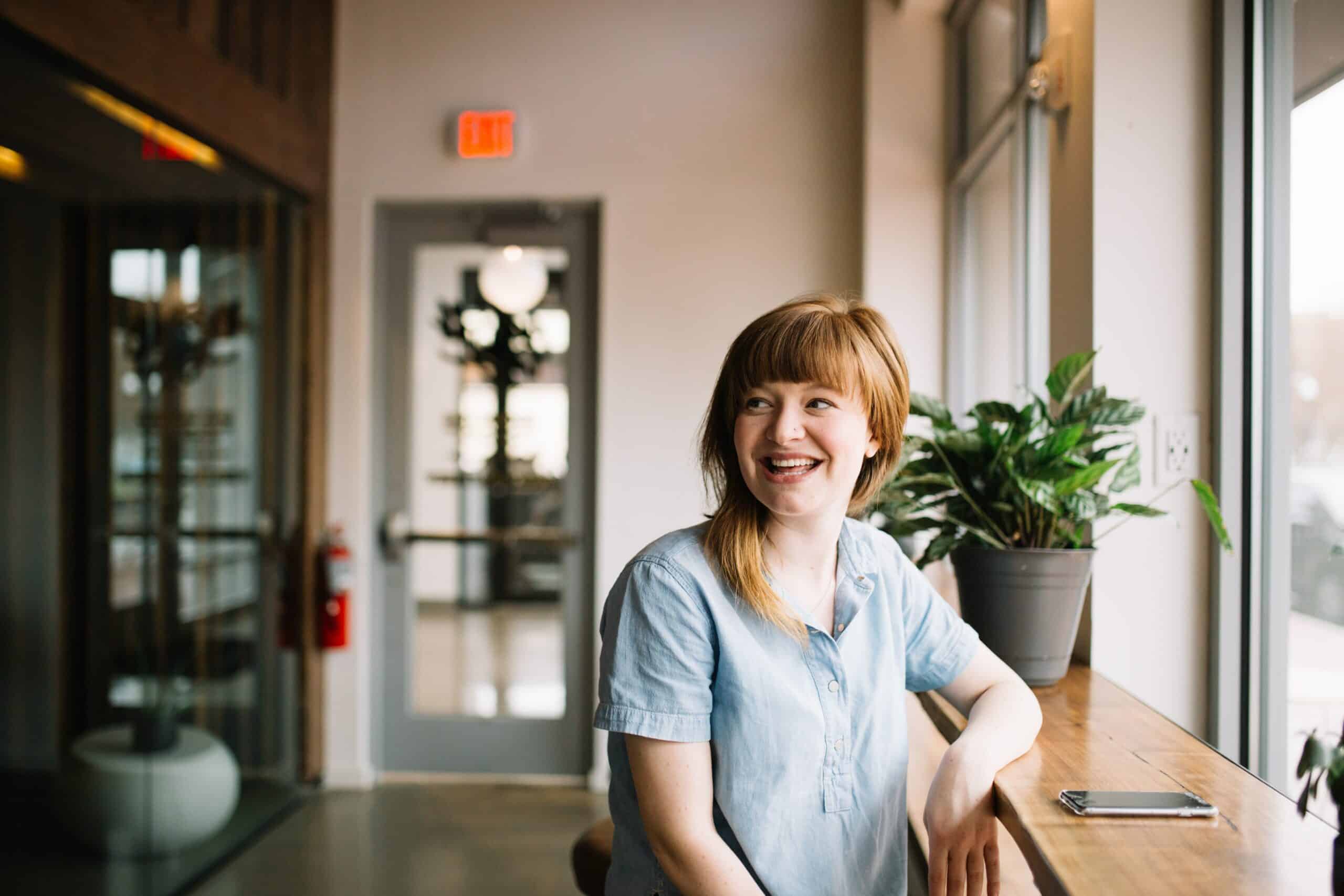 Person with red hair sitting at a high top smiling